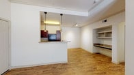 This single-story unit offers a practical and cohesive layout connecting the main living areas through consistent wood-style flooring and neutral wall tones throughout. The living area is spacious and bright, benefiting from natural light through a large window and a patio door, complemented by a ceiling fan overhead. Crown molding adds a refined architectural detail to the main living space.

The kitchen is positioned behind a half-wall pass-through with a granite-style countertop that doubles as a breakfast bar. Inside, rich dark wood cabinetry provides ample storage, paired with granite-style countertops, a double-basin stainless steel sink, and black appliances including a range, microwave, and refrigerator. Pendant lighting and a track light illuminate the kitchen efficiently.

The living area also features a built-in desk nook with granite-style countertop and open shelving, offering a dedicated workspace. The bedroom includes a ceiling fan, a window with natural light, and access to a walk-in closet with built-in shelving. The full bathroom includes a dark wood vanity with a granite-style countertop, tile flooring, and a tub-shower combination with tiled surround.