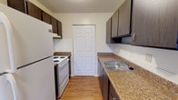 Located at 20 Old Yellow Springs Road in Fairborn, Ohio, this single-floor unit offers a practical and well-organized layout across its living spaces. The kitchen is designed for efficiency, featuring dark espresso-toned cabinetry, granite-look countertops, a stainless steel sink, and white appliances including a refrigerator and electric range. Light hardwood-style flooring runs throughout the kitchen, which also includes a pantry closet for additional storage. The kitchen opens toward the living area, which is finished with wall-to-wall carpeting and ceiling fan, creating a comfortable and cohesive space. The bedrooms are carpeted and feature individual wall-unit air conditioners, baseboard heating, and natural light from exterior-facing windows. Each bedroom includes a closet with panel doors. The unit offers two bathrooms: one equipped with a full tub-shower combo, wood-style flooring, and a white vanity, and a second with a lighted medicine cabinet mirror and white vanity with under-sink storage. Throughout the unit, neutral wall tones and clean finishes provide a move-in ready environment. The overall layout, as visible in the dollhouse view, is open and efficiently organized, making good use of the available footprint.