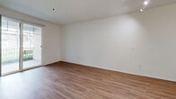 Located at 4161 Keegan St in Dublin, CA, this two-bedroom, one-bathroom residence offers a practical and well-organized single-story layout. The combined kitchen and living room serves as the heart of the home, where warm hardwood-style flooring flows throughout and a sliding glass door opens to a private balcony with outdoor views, filling the space with natural light. The kitchen is efficiently designed with light wood cabinetry extending to the ceiling, generous counter space with a breakfast bar, stainless steel appliances including a gas range, built-in microwave, and refrigerator, plus a double sink. The living area is bright and open, complemented by track lighting near the entryway. Both bedrooms feature plush carpeting and windows that invite natural light; the primary bedroom offers a dedicated closet. The full bathroom is finished with hardwood-style flooring, a soaking tub and shower combination, and clean white surrounds. Overall, the home presents a clean, neutral palette with white walls throughout, creating a bright and move-in-ready environment suited for comfortable everyday living in the Tri-Valley area.