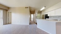 This single-floor residence offers a well-designed, open-concept layout that seamlessly connects the living area and kitchen. The living room is generously sized, finished with plush carpeting, a ceiling fan, and access to a sliding glass door with vertical blinds. The kitchen is outfitted with white shaker-style cabinetry, a subway tile backsplash, light countertops, stainless steel appliances including a refrigerator, and a peninsula with a sink that opens to the living and dining space. A hallway leads to the private quarters, including carpeted bedrooms with ample wall space and natural light. The primary bathroom features a dual-sink vanity with white cabinetry, a large framed mirror with Hollywood-style lighting, white countertops, and rich wood-look flooring. A secondary full bathroom offers a single-sink vanity with matching white cabinetry and the same wood-look flooring. The primary bedroom includes a spacious walk-in closet with built-in shelving and hanging rods on multiple walls. A dedicated laundry room accommodates a full-size washer and dryer with overhead shelving. Throughout the home, neutral tones and clean finishes create a cohesive and move-in-ready atmosphere.