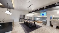 Located in Charlotte, NC, this single-floor entertainment lounge is designed for social gatherings and leisure. The space is anchored by a full-size pool table at its center, positioned atop a dark area rug and illuminated by a pair of large rectangular pendant lights that hang from the vaulted shiplap ceiling. The ceiling's varying heights add architectural dimension, while recessed lighting and a bold black structural beam create a layered, contemporary aesthetic.

The bar area, set beneath a dramatic dropped soffit with warm cove lighting, features sage green cabinetry, a dark countertop, and seating along a bar-height counter with pendant globe lights overhead. Open shelving and textured wall tile complete the refined, lounge-like atmosphere. Adjacent to the bar, a mounted flat-screen TV serves as a focal point for casual viewing.

A dedicated lounge zone offers tufted gray booth-style banquette seating divided into intimate sections, each accompanied by a wall-mounted TV. A game corner with bar-height seating and a large wall-mounted board game adds an interactive element to the space.

Throughout, the herringbone-patterned light wood tile flooring unifies the layout and contributes to the space's clean, modern character. The combination of thoughtful lighting, varied seating options, and well-curated amenities makes this lounge a versatile and inviting gathering destination.