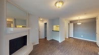 This single-floor unit is designed with a practical, open layout that connects the living, dining, and kitchen areas seamlessly. The living room serves as the focal point, anchored by a white-painted brick fireplace that adds character to the otherwise neutral space. Wood-look plank flooring runs throughout, providing a cohesive and easy-to-maintain surface across all rooms.

The kitchen is accessible via a pass-through counter opening, offering a functional connection to the living area. It features white cabinetry with ample upper and lower storage, dark countertops, a double-basin stainless steel sink, and a black dishwasher. A window above the sink allows natural light to filter in.

The bedrooms are well-proportioned, with one room featuring a window fitted with horizontal blinds, and another offering a full-length sliding glass door covered by vertical blinds, bringing in generous natural light. Both rooms continue the wood-look flooring found throughout.

Storage is well-addressed, with a notable walk-in closet fitted with multiple shelving units and a hanging rod. Textured ceilings are present throughout, and the overall color palette of soft grays and whites lends the space a clean, move-in-ready appearance.