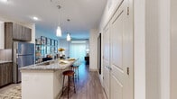 This well-appointed single-floor residence offers a thoughtfully designed open-concept layout with contemporary finishes throughout. The kitchen serves as the heart of the home, showcasing a striking two-tone cabinet design that pairs crisp white upper cabinetry with warm wood-toned lower cabinets. A large granite-topped island with bar seating and elegant pendant lighting anchors the space, while a full suite of stainless steel appliances — including a range, microwave, and refrigerator — provides both style and functionality. Wood-look flooring flows seamlessly from the kitchen into the adjoining living and dining areas, creating a cohesive open feel. The living room offers a comfortable, light-filled retreat with large windows dressed in floor-length curtains that allow natural light to pour in. Each bedroom is generously proportioned, featuring large windows with blinds, soft carpeting, and ample room for substantial furniture. The primary bathroom is finished with large-format tile flooring, a granite vanity with dark wood cabinetry, and direct access to a spacious walk-in closet complete with built-in shelving and hanging systems. Throughout the residence, neutral wall tones, recessed lighting, and clean architectural lines contribute to a modern, inviting ambiance.