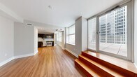 Located at 909 Walnut St in the heart of Kansas City, MO, this modern one-bedroom, one-bathroom unit offers a well-designed layout with contemporary finishes throughout. The open-concept kitchen and living area features warm hardwood flooring, dark espresso cabinetry, granite countertops, and a full suite of stainless steel appliances including a refrigerator, electric range, microwave, and dishwasher. A distinctive split-level design separates the living space, with rich wood-toned steps and a handrail leading to an elevated area bathed in natural light from floor-to-ceiling windows that frame sweeping urban views of the Kansas City skyline. The living room is bright and airy, with clean neutral walls and large windows that fill the space with daylight. The bedroom is carpeted for comfort, featuring multiple windows with city views and a modern sliding wood barn door that opens directly to the bathroom. The bathroom is finished with clean white tile, a soaking tub, pedestal sink, and warm wood-panel doors, lending a spa-like simplicity. A hallway connects the main living areas cohesively. The unit's modern aesthetic, thoughtful split-level architecture, and urban views make it a standout residence in downtown Kansas City.