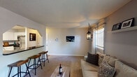 Located at 1105 NC-54 Hwy Bypass in Chapel Hill, NC, this single-floor unit offers a well-organized and functional layout across several thoughtfully designed rooms. The living room serves as the heart of the home, featuring neutral-toned carpet, a textured ceiling, and a decorative pendant light fixture. Natural light filters in through a window fitted with blinds, creating a bright and welcoming atmosphere. A pass-through bar counter with bar stool seating connects the living area to the kitchen, enhancing the open feel of the space. The kitchen is equipped with stainless steel appliances, including a refrigerator, range with microwave overhead, and ample white cabinetry paired with dark countertops and wood-look flooring. The unit includes two bedrooms, each carpeted and outfitted with ceiling fans for comfort. Both rooms feature windows that allow natural light and views of the surrounding greenery. One bedroom benefits from an en-suite bathroom, while the second offers a reach-in closet. The full bathroom features wood-look flooring, a white vanity, and a shower-tub combination. Overall, the unit presents a clean, neutral palette throughout, offering a comfortable and practical living environment in Chapel Hill.