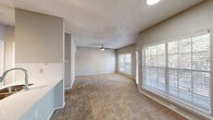 This single-floor residence offers a thoughtfully designed layout that balances comfort and functionality. The open-concept living and dining area is generously sized, featuring neutral-toned carpet, a textured ceiling, and a ceiling fan with light fixture. Multiple windows dressed with white horizontal blinds invite abundant natural light, creating a bright and airy atmosphere throughout the space.

The kitchen is efficiently arranged with a galley-style configuration and showcases stainless steel appliances, including a refrigerator, electric range, and over-the-range microwave. Grey cabinetry, light quartz countertops, and a white subway tile backsplash lend the kitchen a clean, contemporary aesthetic. Wood-look flooring grounds the space with warmth and durability.

The bedroom is comfortably proportioned, also featuring carpet flooring, a ceiling fan, and a window that brings in natural light. A walk-in closet provides ample storage. The adjacent bathroom is split into two distinct areas: a dedicated vanity space with a wide quartz countertop, grey cabinetry, and a well-lit mirror, alongside a separate wet area housing a tiled tub-shower combination, toilet, and additional storage. The space also features a private entry door, contributing to a sense of seclusion and ease of access.