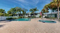 Located at Sun Valley Village in Altamonte Springs, Florida, this outdoor community amenity area centers around a generously sized swimming pool with clear, blue-green water, offering an inviting retreat for residents. The pool is complemented by a circular spa finished with decorative mosaic tile, positioned conveniently nearby on the expansive brick paver deck. The paver surround provides ample space for lounging and socializing, creating a welcoming atmosphere under the Florida sun.

The area is enclosed by a combination of ornamental iron fencing and white vinyl fencing, ensuring both security and a clean, polished appearance. Mature trees — including tall palms and shady oaks — frame the space, providing natural beauty and a degree of shade. Manicured shrubs and landscaped garden beds further enhance the resort-like setting.

A small utility or amenity building with a classic pitched roof sits adjacent to the pool area, finished in neutral tones with French doors. The surrounding residential buildings, featuring green and earth-toned exteriors, are visible in the backdrop and contribute to the cohesive community feel. The entire space benefits from abundant natural light and open skies, making it an ideal outdoor gathering and recreation destination year-round.