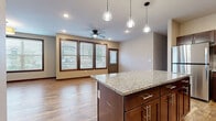 This single-floor residence offers a thoughtfully designed open-concept layout that seamlessly connects the kitchen and living areas. The kitchen is a standout feature, showcasing rich dark-stained cabinetry, a granite-topped center island, stainless steel appliances including a refrigerator, microwave, and range, and open shelving for additional storage. A trio of glass pendant lights illuminates the island, complementing the recessed lighting throughout. Warm hardwood-style flooring extends across the main living and kitchen areas, adding a sense of continuity and warmth.

The living area benefits from an abundance of natural light, provided by a generous bank of windows trimmed in rich dark wood, which also offer views to the outdoors. A ceiling fan keeps the space comfortable year-round. Bedrooms are finished with plush carpeting and feature the same dark wood trim detailing seen throughout the home, lending a cohesive aesthetic. The primary bedroom connects to a spacious walk-in closet equipped with wire shelving systems for organized storage.

A dedicated laundry room houses a full-size front-loading washer and dryer, adding everyday convenience. Neutral wall tones and consistent trim details throughout create a clean, modern, and inviting atmosphere.