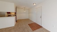 This single-story residence offers a practical and comfortable layout spread across several well-defined areas. The galley-style kitchen is lined with warm wood-toned cabinetry on both sides, providing ample storage, and is equipped with a white electric range, refrigerator, and a stainless steel sink set into a laminate countertop. Durable wood-look flooring runs underfoot, and overhead fluorescent lighting ensures a well-lit workspace. An electrical panel is conveniently located within the kitchen corridor.

The living and dining area transitions from wood-look flooring at the entry to plush wall-to-wall carpeting, creating a cozy atmosphere. A pendant chandelier anchors the dining space, while a six-panel front door serves as the main entry. The living room is highlighted by a full-height sliding glass door dressed with vertical blinds, allowing generous natural light to fill the space with views of surrounding greenery.

The bedroom is generously proportioned with soft carpeting, a window framing outdoor foliage, and direct access to a closet. The bathroom features a warm wood-toned vanity with an integrated sink, a large mirror, a Hollywood-style light bar, and wood-look flooring that extends throughout the hallway, tying the space together cohesively.