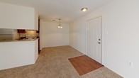 This single-story residence offers a practical and comfortable layout spread across several well-defined areas. The galley-style kitchen is lined with warm wood-toned cabinetry on both sides, providing ample storage, and is equipped with a white electric range, refrigerator, and a stainless steel sink set into a laminate countertop. Durable wood-look flooring runs underfoot, and overhead fluorescent lighting ensures a well-lit workspace. An electrical panel is conveniently located within the kitchen corridor.

The living and dining area transitions from wood-look flooring at the entry to plush wall-to-wall carpeting, creating a cozy atmosphere. A pendant chandelier anchors the dining space, while a six-panel front door serves as the main entry. The living room is highlighted by a full-height sliding glass door dressed with vertical blinds, allowing generous natural light to fill the space with views of surrounding greenery.

The bedroom is generously proportioned with soft carpeting, a window framing outdoor foliage, and direct access to a closet. The bathroom features a warm wood-toned vanity with an integrated sink, a large mirror, a Hollywood-style light bar, and wood-look flooring that extends throughout the hallway, tying the space together cohesively.