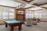 Located at 450 W Orchard Ave in Nampa, Idaho, this expansive single-story community facility offers a generous and well-appointed layout designed to accommodate a variety of social, recreational, and wellness activities. The main entry corridor features striking slate tile flooring, warm red wood baseboards, and soft wall sconces, leading residents through the space via elegant French doors with rich wood trim accents.

The heart of the facility is a spacious clubroom, where beamed ceilings with track lighting, large windows flooding the room with natural light, and a classic fireplace create a welcoming atmosphere. High-top tables with bar stools invite casual gathering, while a billiards table adds a recreational focal point. Adjacent is a comfortable lounge area with plush seating and a large flat-screen TV, ideal for relaxed entertainment.

A well-equipped fitness center features vaulted ceilings, full-wall mirrors, fluorescent lighting, and an array of cardio and strength-training equipment, including treadmills, ellipticals, and cable machines. A secondary exercise area with open carpeted space and a vending machine provides additional flexibility.

The kitchenette offers granite countertops, rich cherry cabinetry, stainless steel appliances, and a breakfast bar — perfect for casual refreshments. Smaller private rooms with carpet, skylights, and neutral tones provide quiet spaces for meetings or individual use.