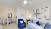 Located at 100 Millspring Dr in Durham, North Carolina, this single-floor residence offers a well-designed layout with a comfortable and cohesive living environment. The living room serves as the heart of the home, showcasing a ceiling fan with light fixture, light-toned carpeting, and crisp white walls that create a clean, airy atmosphere. Framed artwork adorns the walls, adding a decorative touch to the neutral palette. The space flows naturally into adjacent areas of the home, with an open passageway visible from the main living area leading toward what appears to be a hallway and additional rooms. A separate dining area is partially visible, featuring a bistro-style table and chairs, indicating a distinct and functional dining space. The layout promotes easy movement throughout the home, with well-defined zones for living and dining. Natural and artificial lighting work together to keep the interior bright and welcoming. Overall, the residence presents a tidy, move-in-ready feel with a practical single-floor plan suited for comfortable everyday living in the Durham area.