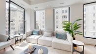 Located on prestigious Rue Sherbrooke Ouest in Montréal, this contemporary 2-bedroom, 2-bathroom residence showcases a refined modern aesthetic defined by clean lines, crisp white walls, and light hardwood flooring throughout. The open-concept living area is anchored by large floor-to-ceiling windows with black frames, bathing the space in abundant natural light while offering views of the surrounding cityscape. The sleek kitchen features flat-front white cabinetry extending to the ceiling, a white quartz waterfall island with bar seating, a matte black faucet, and stainless steel appliances including a French door refrigerator and integrated dishwasher. The living room benefits from multiple oversized windows that frame the urban streetscape, creating a bright and airy atmosphere. A clean, minimalist corridor connects the private quarters, where both bedrooms continue the light, neutral palette with generous closet space. The primary bedroom enjoys a large window with city views. Both bathrooms are elegantly appointed with large-format porcelain tile flooring, white floating vanities, illuminated mirrors, and glass-enclosed walk-in showers accented with matte black hardware — a cohesive and sophisticated finishing touch carried throughout the entire residence.
