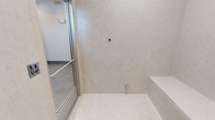 This contemporary bathroom space is defined by its refined, minimalist design and high-quality finishes throughout. The walls are clad in fine mosaic tiles in a soft, neutral cream palette, extending from floor to ceiling to create a seamless and cohesive visual flow. The large-format floor tiles echo the same light tones, reinforcing the clean and airy atmosphere of the room.

A frameless or slim-profile glass door serves as the enclosure for the shower area, allowing light to pass freely through the space while maintaining a modern, open feel. Inside the shower, a built-in tiled bench provides both a practical and architectural element, blending smoothly with the surrounding tile work.

Subtle chrome or brushed-metal hardware accents are visible, including a towel bar and plumbing fixtures, complementing the neutral tones without overpowering the understated elegance of the design. The linear floor drain adds a contemporary touch while ensuring clean, functional drainage.

Overall, the space exudes a spa-like quality, with its consistent material palette, precise tile work, and thoughtful layout. The combination of natural-toned tiles, glass elements, and minimalist hardware creates an environment that feels both sophisticated and tranquil.