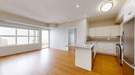 This single-floor residence offers a thoughtfully organized layout across two bedrooms, one bathroom, and a combined kitchen and living area. Warm hardwood-style flooring runs consistently throughout the unit, creating a cohesive and inviting aesthetic in every room.

The open-concept kitchen and living area forms the heart of the home. The kitchen is outfitted with white shaker-style cabinetry, a gray tile backsplash, stainless steel appliances including a refrigerator and range, and a granite-topped island with an integrated sink. The island also functions as a breakfast bar, bridging the kitchen and living space seamlessly. The living area benefits from large windows and a glass-paneled balcony door that floods the space with natural light.

Both bedrooms are bright and well-proportioned, each featuring large windows that invite natural light. Each bedroom is accompanied by a dedicated closet for ample storage. The primary bedroom offers a comfortable footprint suitable for standard furnishings.

The bathroom features a granite-topped vanity with an undermount sink, white cabinetry with ample storage, a large mirror, and a shower-tub combination. The overall design maintains a clean, neutral palette throughout, lending the space a modern and functional character.