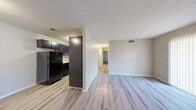 This single-floor unit offers a practical and efficiently designed layout, accommodating two bedrooms and two full bathrooms. The open-concept living and kitchen area serves as the heart of the space, where light gray vinyl plank flooring extends throughout, creating a cohesive and clean aesthetic. The kitchen is fitted with dark espresso cabinetry, black appliances including a full-size refrigerator and range, a U-shaped counter configuration, and a flush-mount ceiling light. A tall pantry-style cabinet provides additional storage at the kitchen's entry point.

The living area benefits from a large sliding glass door dressed with vertical blinds, allowing generous natural light to fill the room. A central hallway connects the living space to the two bedrooms and bathrooms. Each bedroom features the same vinyl plank flooring, neutral wall tones, a textured ceiling, and windows that admit natural light. One bedroom includes a sliding glass door, while the other features a standard window. The bathrooms are finished with white tub-shower combinations, light countertops, and dark-framed vanity mirrors. Throughout the unit, a consistent textured ceiling, neutral palette, and clean finishes contribute to a functional, move-in-ready ambiance.
