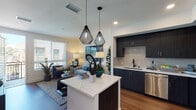 Located at 9840 Carroll Canyon Rd in San Diego's Scripps Ranch neighborhood, this contemporary single-floor residence offers a thoughtfully designed open-concept layout. The kitchen is a standout feature, showcasing dark espresso cabinetry, a textured tile backsplash, light quartz countertops, and a full suite of stainless steel appliances including a gas range, dishwasher, microwave, and refrigerator. A large waterfall-edge island with seating for two anchors the space, illuminated by a pair of striking geometric black pendant lights. Warm hardwood-style flooring flows throughout the main living areas, connecting the kitchen seamlessly to the living room. The living area benefits from generous natural light through large windows with views of the surrounding neighborhood. The bedroom is a serene retreat featuring plush carpeting, a window with outdoor views, and warm ambient lighting. The bathroom is finished with a dark vanity, white quartz countertop, and an oversized mirror. A conveniently tucked-away hallway closet houses a stacked in-unit washer and dryer. Clean neutral walls and recessed lighting throughout contribute to a modern, cohesive aesthetic.