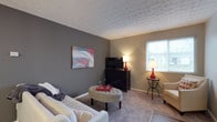 Located at 1075 Weybridge Rd in Columbus, Ohio, this single-floor residence offers a comfortable and well-appointed living environment in the 43220 zip code. The living area showcases a thoughtful design with a warm, neutral color palette, combining soft gray and beige tones across the walls and carpeted flooring. A textured ceiling adds visual interest and depth to the room, complementing the understated yet stylish aesthetic throughout. Natural light filters in through a window dressed with blinds, brightening the space and creating an inviting atmosphere. The room provides ample space for relaxed living, with a layout that accommodates seating, a media console, and accent furnishings with ease. The overall ambiance of this residence is calm and welcoming, with a cohesive design sensibility that balances comfort and function. Its single-floor layout ensures easy accessibility and a seamless flow throughout the home, making it well-suited for a variety of lifestyles.
