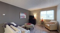 Located at 1075 Weybridge Rd in Columbus, Ohio, this single-floor residence offers a comfortable and well-appointed living environment in the 43220 zip code. The living area showcases a thoughtful design with a warm, neutral color palette, combining soft gray and beige tones across the walls and carpeted flooring. A textured ceiling adds visual interest and depth to the room, complementing the understated yet stylish aesthetic throughout. Natural light filters in through a window dressed with blinds, brightening the space and creating an inviting atmosphere. The room provides ample space for relaxed living, with a layout that accommodates seating, a media console, and accent furnishings with ease. The overall ambiance of this residence is calm and welcoming, with a cohesive design sensibility that balances comfort and function. Its single-floor layout ensures easy accessibility and a seamless flow throughout the home, making it well-suited for a variety of lifestyles.