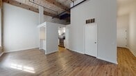 Located at 303 Vine St in Philadelphia, PA, this single-floor unit showcases a compelling blend of historic character and modern updates. The open living area immediately impresses with soaring ceilings featuring exposed wooden beams and visible ductwork, lending a distinctive industrial-loft aesthetic. Warm hardwood flooring runs throughout, complementing the raw textures of the space.

A standout feature is the exposed brick column in the bedroom area, which adds a rich, historic element against the neutral gray accent wall. Natural light pours in through large windows, enhancing the airy, open feel of the space.

The kitchen is cleanly designed with white shaker-style cabinetry, sleek bar-pull hardware, light quartz countertops, and stainless steel appliances including a built-in microwave and electric range. A pass-through counter connects the kitchen to the main living area, improving both flow and functionality.

A narrow hallway with black iron pipe detailing leads to additional areas of the unit, including carpeted stair access. The bathroom is finished in a clean, classic style with a full tub-shower combination, mosaic tile flooring, a large vanity mirror, and a quartz-topped vanity with under-sink storage. Overall, the space delivers an urban, character-rich living environment rooted in Philadelphia's architectural heritage.