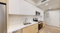 Located at 139 S Occidental Blvd in Los Angeles, this efficiently designed single-floor unit offers a thoughtfully organized layout making excellent use of its compact footprint. The interior features a clean, modern aesthetic defined by crisp white walls, light wood-tone luxury vinyl flooring, and recessed lighting throughout.

The kitchen is a standout feature, showcasing a galley-style configuration with flat-front cabinetry in a two-tone combination of white upper cabinets and warm natural wood lower cabinets. Sleek white quartz countertops run the length of the kitchen, complemented by a stainless steel sink, stainless steel refrigerator, electric range, and an over-the-range microwave. A window at the end of the kitchen allows natural light to filter into the open living area beyond.

The bathroom maintains the same contemporary palette, featuring large-format light tile flooring, a wood-toned vanity with a white countertop, a full-width mirror, and clean white walls that lend a bright, airy feel to the space.

A dedicated laundry area houses a stacked full-size washer and dryer unit, providing practical in-unit convenience. The overall design of this Los Angeles residence emphasizes modern minimalism, efficient use of space, and quality finishes throughout.