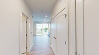 This single-floor unit offers a thoughtfully designed layout finished with contemporary materials throughout. Light wood-toned luxury vinyl plank flooring runs continuously across the space, complementing the clean white walls and recessed lighting that keep the interior bright and welcoming.

The kitchen is a standout feature, equipped with a full suite of stainless steel appliances including a range, over-the-range microwave, refrigerator, and dishwasher. Two-toned cabinetry pairs white upper cabinets with dark wood-grain lower cabinets, accented by a white subway tile backsplash and light quartz countertops. The design is both functional and visually sharp.

A hallway connects the main living area to the private spaces, including a bedroom with a closet and access to storage. The living area benefits from generous natural light through a large sliding glass door that opens to a balcony with outdoor views.

The full bathroom features marble-style tile flooring, a glass-enclosed shower, a toilet, and a dark wood-grain vanity topped with a white surface and accompanied by a large mirror. The overall design maintains a clean, modern aesthetic consistent throughout the unit.