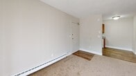 Located at 881 44th St SW in Wyoming, Michigan, this single-floor, one-bedroom unit offers a functional and straightforward layout designed for comfortable everyday living. The living room is carpeted and bathed in natural light through a full-width sliding glass door fitted with vertical blinds, which opens to an outdoor view of surrounding greenery. A wall-mounted air conditioning unit and baseboard heating ensure year-round climate control. The entryway transitions from hardwood-style flooring into the carpeted living space, with a clear sightline toward the kitchen area, which features wood-toned cabinetry and a gas range. The bedroom is a well-proportioned retreat, also finished with plush carpeting and neutral walls. It benefits from a standard window that brings in natural light and includes two closets — one a standard reach-in closet with shelving and one that leads to an additional storage space — providing generous storage for the room's size. Throughout the unit, the design is clean and practical, with textured ceilings, white trim, and a consistent neutral color palette that creates a calm, cohesive atmosphere. Baseboard heaters are present throughout, complementing the overall utilitarian yet comfortable character of this Wyoming, MI residence.