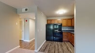 This single-floor residence offers a thoughtfully designed layout that balances functionality and comfort. The kitchen serves as a practical hub, featuring warm honey-toned wood cabinetry with ample upper and lower storage, dark granite-style countertops, and a full suite of black appliances including a refrigerator, electric range, and built-in oven. Wood-look vinyl plank flooring runs throughout the kitchen and entry areas, providing a durable and attractive foundation. The layout opens toward a hallway corridor that connects the main living areas seamlessly. The bedrooms are generously sized, finished with plush wall-to-wall carpeting and painted in soft, neutral gray-green tones that create a calm and restful atmosphere. Natural light filters in through windows offering views of surrounding greenery. At least one bedroom includes a sliding-door closet with built-in shelving and hanging space, offering practical storage. The bathroom is cleanly appointed with white cabinetry, a dark stone-patterned countertop, a single vanity sink, and a full soaking tub with shower surround. Consistent white trim and neutral wall tones tie the entire space together, creating a cohesive, move-in-ready environment throughout.