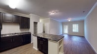 Located at 11101 Beckstone Way in Wake Forest, NC, this single-story residence offers a well-designed, open-concept layout that connects the kitchen and living areas seamlessly. The kitchen is a standout feature, equipped with rich dark cabinetry, bold dark stone countertops with gold veining, black appliances including a range, microwave, refrigerator, and dishwasher, and a double-basin sink. A central island with matching countertop provides additional prep and storage space, while a dedicated pantry with built-in shelving adds further functionality. Crown molding accents the kitchen and living area ceilings, lending an elevated finish throughout. The living room is bright and open, with hardwood-style flooring, a ceiling fan, and glass doors that invite natural light and outdoor views. The bedrooms feature plush carpeting and ceiling fans, offering a comfortable retreat. A spacious walk-in closet provides generous storage with wire shelving systems. The bathrooms include full tub-shower combinations with curved curtain rods, tile flooring, and clean white fixtures. Built-in open shelving near the entry adds a practical organizational touch, completing this cohesive and functional living space.