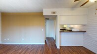 Located at 2345 N Craycroft Rd in Tucson, Arizona, this single-floor unit offers a straightforward and functional layout designed for comfortable everyday living. Rich wood-style flooring runs consistently throughout the space, providing a warm and cohesive aesthetic from room to room.

The open living area is defined by a combination of painted walls in warm neutral tones and a distinctive white brick accent wall, adding textural character to the space. A textured ceiling complements the overall design. A sliding glass door floods the living area with natural light and provides access to an outdoor balcony, offering views of the surrounding Tucson neighborhood.

The kitchen is situated adjacent to the living area and is accessible via a pass-through counter with a dark laminate surface. White cabinetry with raised-panel doors provides ample storage, while a white brick tile backsplash and electric range complete the functional cooking space. The kitchen's open connection to the main living area enhances the overall sense of space.

A hallway leads to the private areas of the unit, including the bathroom, which features a full tub and shower combo with clean white surround panels, a grab bar, and a small window that allows in natural light. The unit includes central HVAC with ceiling vents throughout, ensuring year-round comfort in the Tucson climate.