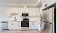 This well-appointed one-bedroom, one-bathroom unit at 2002 N Monroe St, Unit 405, in Spokane, Washington, offers a thoughtfully designed layout with modern finishes throughout. Light wood-style flooring flows seamlessly across the entire space, creating a clean, cohesive aesthetic.

The kitchen is a standout feature, showcasing crisp white cabinetry with matte black hardware, a full suite of stainless steel appliances including a refrigerator, electric range, and over-the-range microwave, and a deep undermount sink. Ample upper and lower cabinet storage makes the kitchen as functional as it is visually appealing.

The open living area provides a comfortable, light-filled space with clean white walls and a neutral palette that offers versatile styling options. The bedroom is generously sized, featuring large windows that invite natural light and offer pleasant views of the surrounding neighborhood.

The bathroom is finished with a white vanity, a bold circular black-framed mirror, chrome fixtures, and a shower-tub combo, delivering a clean and contemporary feel. An in-unit laundry area includes a stacked full-size washer and dryer along with wire shelving for additional storage. This unit combines modern design with practical functionality in a well-located Spokane address.
