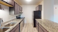 Located at 616 W Bridge St in Owatonna, Minnesota, this single-floor unit offers a well-organized layout with a clean, neutral aesthetic throughout. The living area features light wood-style flooring and a sliding glass door that opens onto a private balcony, allowing natural light to fill the space while providing a pleasant outdoor view. A wall-mounted air conditioning unit and baseboard heating ensure year-round comfort.

The galley-style kitchen is thoughtfully appointed with dark espresso cabinetry, granite countertops, and stainless steel appliances, including an electric range and refrigerator, all set on light wood-style flooring. The textured ceiling adds subtle character to the space.

The bedrooms are finished with wall-to-wall carpet for added warmth and comfort, each room equipped with a ceiling fan and a window that brings in natural light and views of the surrounding greenery. Baseboard heating is present throughout.

The bathroom offers a cohesive design that mirrors the kitchen's finishes, featuring a granite-topped vanity with a dark wood cabinet base, a full tub-shower combination with clean white surround, and light wood-style tile flooring. Overall, the unit presents a consistent, updated interior with practical amenities suited for comfortable everyday living.