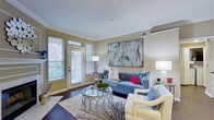 This single-floor residence is thoughtfully designed with a cohesive aesthetic that blends comfort and style across its living spaces. The living room serves as the heart of the home, showcasing rich hardwood flooring, elegant crown molding, and a tile-surround fireplace flanked by a full-light exterior door that invites generous natural light. A large-format abstract artwork anchors the main wall, complementing the space's contemporary character.

Adjacent to the living area, a secondary space features built-in shelving and an additional fireplace, offering versatility as a sitting room or study. A large mirror installation in the dining area visually expands the space, which accommodates a round table with lattice-back chairs and warm wood flooring underfoot.

The kitchen is outfitted with warm honey-toned cabinetry, white countertops, tile flooring, and a full suite of appliances, with a pass-through opening connecting it to the dining and living areas. The bedroom provides a serene retreat with plush carpeting, a wide window with outdoor views, and a ceiling fan. The full bathroom features a dual-sink white vanity, tile flooring, and a glass-enclosed shower-tub combination, completing this well-rounded residence.