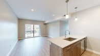 This well-designed 2-bedroom, 2-bathroom residence in Troy, Michigan offers a thoughtful layout with modern finishes throughout. The open-concept living and kitchen area serves as the heart of the home, featuring light wood-tone flooring, recessed lighting, and a sliding glass door that opens to a private balcony with outdoor views. The kitchen is appointed with custom wood-grain cabinetry, quartz countertops, a peninsula island with an undermount sink and pendant lighting, and a full suite of stainless steel appliances including a gas range, microwave, and refrigerator, complemented by a subway tile backsplash. The spacious primary bedroom is bathed in natural light from multiple large windows and features plush carpeting and a ceiling fan. The second bedroom also enjoys generous natural light through a large window with scenic outdoor views. Both bathrooms echo the home's modern aesthetic, with wood-grain vanities, quartz countertops, and neutral tile flooring. A dedicated closet provides convenient storage. Neutral wall tones and clean architectural lines create a cohesive, contemporary ambiance throughout this well-appointed Troy residence.