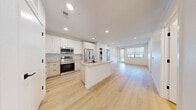 Located at 18307 E 51st Ave in Denver, CO, this modern 2-bedroom, 2-bathroom residence offers a thoughtfully designed open-concept layout with clean, contemporary finishes throughout. Light hardwood flooring flows through the main living areas, contrasting beautifully with plush carpeting in the bedrooms. The kitchen is a standout feature, boasting white and natural wood-tone cabinetry reaching to the ceiling, a large center island with an undermount sink, stainless steel appliances including a French door refrigerator, range, and microwave, complemented by a textured tile backsplash. The kitchen opens seamlessly into the spacious living area, which is bathed in natural light and provides direct access to a private balcony. Both bathrooms are finished with light wood-tone vanities, matte black hardware, large mirrors, and light wood flooring. The primary bathroom features a dual-sink vanity and a walk-in glass shower, while the second bathroom offers a full soaking tub. The generously sized primary bedroom includes a walk-in closet with built-in shelving. The unit also features four closets in total and a convenient in-unit laundry area, rounding out a well-appointed and functional living space.