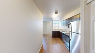 Located at 390 E Main St in Hillsboro, Oregon, this efficiently designed single-floor unit offers a well-organized layout that maximizes every inch of its compact footprint. The open-plan kitchen and living area form the heart of the space, with light wood-style flooring running continuously throughout, creating a cohesive and airy feel.

The kitchen is thoughtfully appointed with rich dark-wood cabinetry extending to the upper walls for ample storage, complemented by crisp white countertops and a full suite of stainless steel appliances, including a refrigerator, electric range, built-in microwave, and dishwasher. A single-basin sink with a window above brings in natural light to the work area.

The living area is bright and open, benefiting from large windows fitted with horizontal blinds that allow for adjustable natural light and views of the surrounding Hillsboro neighborhood. A wall-unit HVAC system provides climate control, and access to an exterior door adds convenience.

The bathroom features a wide vanity with a single sink, generous white countertop surface, a large mirror, and dark cabinetry below. An adjacent walk-in closet with wire shelving provides practical storage. Textured ceilings are present throughout the unit, adding a subtle architectural detail to the otherwise clean, neutral-toned interior.