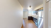 Located at 390 E Main St in Hillsboro, Oregon, this efficiently designed single-floor unit offers a well-organized layout that maximizes every inch of its compact footprint. The open-plan kitchen and living area form the heart of the space, with light wood-style flooring running continuously throughout, creating a cohesive and airy feel.

The kitchen is thoughtfully appointed with rich dark-wood cabinetry extending to the upper walls for ample storage, complemented by crisp white countertops and a full suite of stainless steel appliances, including a refrigerator, electric range, built-in microwave, and dishwasher. A single-basin sink with a window above brings in natural light to the work area.

The living area is bright and open, benefiting from large windows fitted with horizontal blinds that allow for adjustable natural light and views of the surrounding Hillsboro neighborhood. A wall-unit HVAC system provides climate control, and access to an exterior door adds convenience.

The bathroom features a wide vanity with a single sink, generous white countertop surface, a large mirror, and dark cabinetry below. An adjacent walk-in closet with wire shelving provides practical storage. Textured ceilings are present throughout the unit, adding a subtle architectural detail to the otherwise clean, neutral-toned interior.