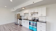 This thoughtfully designed single-floor unit showcases a clean, contemporary aesthetic throughout. The kitchen is a standout feature, outfitted with white shaker-style cabinetry, dark granite countertops, and a classic white subway tile backsplash. Stainless steel appliances — including a refrigerator, dishwasher, and a uniquely accented range — complete the space with both function and style. A long, bright hallway with recessed lighting connects the kitchen to the rest of the unit, guiding residents through the thoughtfully laid-out floor plan. The bedrooms are generously proportioned, each featuring light wood-style flooring, crisp white walls, and large double-hung windows that invite abundant natural light and views of the surrounding greenery and neighborhood. Multiple bedrooms include dedicated closet space, offering practical storage solutions. The bathroom is elegantly finished with large-format marble-look tile on both the floors and the tub surround, creating a spa-like atmosphere. A soaking tub with an overhead shower and a natural light-filled window round out this serene retreat. Light wood flooring flows consistently throughout the unit, tying together the modern, airy, and cohesive design of this well-appointed space.