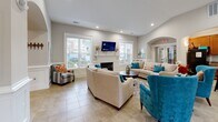 Located at 17 Lyndhurst Ave in Asheville, NC, this single-floor community clubhouse offers a thoughtfully designed layout that balances functionality with a warm, inviting ambiance. The space is unified by light-toned ceramic tile flooring throughout and crisp white wainscoting that lends a polished, cohesive aesthetic.

The reception area serves as the central hub, featuring an elegant arched counter with warm wood cabinetry, pendant lighting, and wide arched doorways that frame the entry and connect the space gracefully. Adjacent to the reception is a comfortable lounge area anchored by a classic white fireplace with a mounted television above, surrounded by neutral upholstered seating accented with teal and coral throw pillows, creating a relaxed yet refined gathering space.

A dedicated office area benefits from an abundance of natural light, with multiple windows dressed in bold rust-red curtains that add a striking pop of color. The space also includes a creative corner adorned with a lush vertical green wall and decorative accents, adding a vibrant, artistic touch.

The kitchenette is well-equipped with rich wood cabinetry, granite countertops, a double basin sink, and full-size refrigerator, providing practical amenities for residents and guests alike. Recessed lighting throughout ensures a bright, welcoming atmosphere at all times.