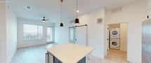 This contemporary 1020 square foot apartment offers a well-designed living space with two bedrooms and two bathrooms. The open-concept layout seamlessly integrates the kitchen and living areas, creating a spacious feel. The kitchen is a standout feature, boasting two-tone cabinetry with white upper cabinets and striking blue lower cabinets. A large island with a light-colored countertop provides additional workspace and casual dining. Stainless steel appliances, including a side-by-side refrigerator, complete the modern aesthetic.

The primary bedroom, measuring 180 square feet, features plush carpeting and a ceiling fan for comfort. Large windows in the bedrooms and living areas flood the space with natural light and offer city views. The bathrooms showcase contemporary design with sleek fixtures, ample counter space, and a glass-enclosed shower.

A dedicated laundry room with full-sized, stacked washer and dryer units adds convenience. The apartment also includes well-designed closet spaces with built-in shelving and hanging rods. Throughout the unit, you'll find a mix of carpeting in the bedrooms and stylish wood-look flooring in the main living areas, creating a cohesive and modern ambiance. The neutral color palette and clean lines contribute to the apartment's fresh, inviting atmosphere.