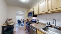 This single-floor, 2-bedroom, 1-bathroom residence offers a functional and comfortable layout across a generous footprint. The entry flows into a galley-style kitchen featuring light maple cabinetry, granite-style countertops, stainless steel appliances including a gas range, microwave, dishwasher, and refrigerator, all set atop wood-look flooring. The kitchen opens conveniently into a dedicated dining area highlighted by a bold blue accent wall, pendant chandelier lighting, and a window with a valance treatment.

The living room provides a spacious and bright gathering area with carpet flooring, a large window with views of surrounding greenery, and ample room for comfortable furnishings. The primary bedroom is a well-sized retreat with plush carpet, neutral tones, and access to a walk-in closet with dual hanging rods and built-in shelving. The second bedroom offers flexibility as a home office or guest room, also featuring carpet flooring and a windowed door for natural light. The full bathroom includes a single vanity with a wood cabinet base, an oval mirror, and a shower/tub combination. Textured ceilings are consistent throughout, adding architectural character to this well-rounded home.