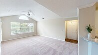 This 2-bedroom, 1-bathroom home delivers a thoughtfully organized single-floor layout designed for comfortable living. The living room is a standout space, featuring dramatic vaulted ceilings, a ceiling fan, and a striking arched window above a large picture window that floods the room with natural light and offers views of lush greenery outside. Soft carpeting and neutral-toned walls create a warm, inviting atmosphere throughout. The kitchen is well-appointed with white shaker-style cabinetry, granite countertops, a subway tile backsplash, stainless steel appliances including a refrigerator and dishwasher, and a breakfast bar peninsula that opens to the living and dining areas. Hardwood-style flooring anchors the kitchen and entry. The primary bedroom is generously sized, complete with a ceiling fan, carpeted flooring, and a walk-in closet outfitted with wire shelving for organized storage. The second bedroom also features a ceiling fan and a window with outdoor views. The shared bathroom includes a granite-topped vanity with white cabinetry, a large mirror, and a shower/tub combination. A dedicated in-unit laundry area with a washer and overhead shelving adds everyday convenience, rounding out this functional and comfortable home.