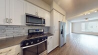 Located at 4560 Mission Gorge Place in San Diego, CA, this single-floor residence offers a thoughtfully designed layout with contemporary finishes throughout. The kitchen is a standout feature, showcasing white shaker cabinetry, dark countertops, a subway tile backsplash, and a full suite of stainless steel appliances including a gas range, over-the-range microwave, French door refrigerator, and dishwasher. A central island with pendant lighting adds both workspace and visual appeal, while the open sightlines connect the kitchen seamlessly to the spacious living area, which features warm hardwood-style flooring and a ceiling fan. The bedrooms are finished with plush carpeting, large windows dressed with horizontal blinds that invite natural light, and access to well-sized closets with built-in shelving. The bathrooms are elegantly appointed with large-format marble-style tile flooring, white vanities, and generous mirrors. One bathroom includes a soaking tub with a subway tile surround and a wall-mounted storage cabinet, while another connects to a walk-in closet. The unit also includes in-unit laundry. Clean neutral tones and modern hardware throughout create a cohesive, contemporary aesthetic.