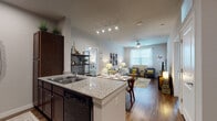 This single-floor residence offers a thoughtfully designed open-concept layout that seamlessly connects the kitchen, dining, and living areas. The kitchen is well-equipped with rich dark cabinetry, granite countertops, a double-basin sink, black appliances including a refrigerator and dishwasher, and generous storage throughout. A peninsula counter provides casual seating and flows naturally into the dining space. The living room is bright and welcoming, featuring hardwood-style flooring, a ceiling fan, and large windows that allow abundant natural light to fill the room. The primary bedroom is a comfortable retreat with a large window, hardwood-style flooring, and direct access to an en-suite bathroom. The primary bath includes a soaking tub, a dark-wood vanity, and a walk-in closet with built-in shelving and hanging storage. The second bedroom features plush carpeting, a generous window with sheer curtains, and ample space. A second full bathroom mirrors the quality finishes of the primary bath, with a tub-shower combination, dark cabinetry, and hardwood-style flooring. Neutral tones and consistent finishes throughout create a cohesive and modern ambiance across the entire residence.