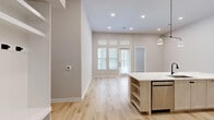 Located in Plano, TX, this well-appointed single-story home offers three bedrooms, two bathrooms, and five closets within a thoughtfully designed open-concept floor plan. The combined kitchen and living area serves as the heart of the home, featuring light wood-look flooring, recessed lighting, and elevated ceilings that create an airy, spacious feel. Large windows and a glass-paneled front door invite abundant natural light throughout. The kitchen is outfitted with light wood cabinetry, white quartz countertops, a subway tile backsplash, stainless steel appliances, and a center island with built-in shelving. The primary bedroom is generously sized, featuring tall windows with transom panels that maximize natural light, and is complemented by a walk-in closet with built-in shelving and hanging rods. The primary bathroom is a standout, showcasing marble-style tile, a glass-enclosed walk-in shower, a soaking tub, dual-sink vanity with matte black fixtures, and direct access to the walk-in closet. Secondary bedrooms share the same warm flooring and neutral palette. Throughout the home, a consistent modern aesthetic ties together clean lines, soft neutral tones, and quality finishes.