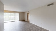 This single-floor residence offers a straightforward and functional layout across several well-defined living spaces. The living area is bright and open, featuring smooth gray-toned hardwood-style flooring and neutral walls that create a clean, versatile backdrop. A full-length sliding glass door fitted with vertical blinds allows generous natural light to flow in while providing direct access to an outdoor area with greenery views, enhancing the sense of openness.

The kitchen is efficiently laid out with warm oak cabinetry, laminate countertops, a double stainless steel sink, and a white refrigerator. A dedicated entry door in the kitchen provides convenient secondary access to the unit.

The bedrooms are carpeted in a neutral tone and each feature a ceiling fan with light fixture, offering comfort year-round. Windows in each bedroom frame leafy outdoor views, contributing to a calm and airy atmosphere throughout.

The bathroom is finished in crisp white tile from the tub surround to the walls, and includes a combination tub and shower with a handheld showerhead, chrome grab bars for added safety, a toilet, and white cabinetry for storage. A frosted window above the tub provides natural light while maintaining privacy.

Overall, this residence presents a clean, practical, and move-in-ready space with consistent neutral finishes throughout.