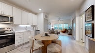 This thoughtfully designed one-bedroom, one-bathroom residence maximizes its single-floor layout with an open-concept kitchen and living area that flows seamlessly from one end to the other. The kitchen features crisp white shaker cabinetry extending to the ceiling, a classic subway tile backsplash with under-cabinet lighting, and a full suite of stainless steel appliances including a side-by-side refrigerator, dishwasher, and range. A round dining table positioned at the kitchen's edge provides a casual yet functional dining space. Light wood-style flooring runs throughout the main living areas, enhancing the bright, airy atmosphere. The living room is anchored by a bank of large windows that frame lush greenery views and flood the space with natural light, complemented by a ceiling fan overhead. The bedroom offers a quiet retreat with carpet flooring, a window with outdoor views, and a closet with double doors. The full bathroom is clean and functional, featuring a white vanity and a tub-shower combination. Recessed lighting and a neutral white palette throughout create a cohesive, modern aesthetic that is both inviting and practical.