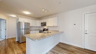 Located at 1 Ari Dr in Westbrook, Maine, this well-appointed 2-bedroom, 1-bathroom residence offers a thoughtfully designed single-floor layout. The open-concept kitchen and living area serves as the heart of the home, featuring white shaker cabinetry, granite countertops, a peninsula with an undermount sink, and a full suite of stainless steel appliances including a range, microwave, dishwasher, and refrigerator. Track lighting and light wood-tone flooring throughout the main living areas create a clean, contemporary aesthetic. The living room is bright and spacious, enhanced by a wall-mounted mini-split system for efficient climate control. The primary bedroom is generously sized, filled with natural light from large windows that frame views of surrounding woodland, and includes a walk-in closet. The second bedroom features plush carpeting and a sliding-door closet. The full bathroom is finished with a white vanity, under-cabinet storage, and wood-look flooring. A dedicated laundry room houses a full-size top-loading washer and dryer with overhead shelving. The overall design is clean, modern, and move-in ready, offering comfortable and functional living in a natural Maine setting.