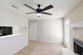Located at 12400 Jefferson Hwy in Baton Rouge, Louisiana, this two-bedroom, two-bathroom single-floor residence offers a well-organized layout designed for comfortable everyday living. The combined living room and kitchen area serves as the heart of the home, where a tile-surround wood-burning fireplace with a white mantel becomes an immediate focal point. Light wood-style flooring runs throughout the space, complementing the neutral, warm-toned walls and creating a cohesive aesthetic. Ceiling fans are present in the living area and both bedrooms, providing practical comfort. The living room benefits from multiple windows fitted with horizontal blinds, allowing natural light to fill the room. A half-wall pass-through connects the living area to the kitchen, which features sage-toned cabinetry, light countertops, a built-in range, and a full-size refrigerator. A hallway leads from the living area to both bedrooms, each offering a ceiling fan and a window with natural light. The primary bedroom includes access to a bathroom featuring a full soaking tub and vanity with cabinetry. A second bathroom serves the additional bedroom. A dedicated closet provides storage, and light wood-style flooring extends seamlessly through the hallways and bedrooms, unifying the entire floor plan.