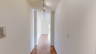 This 1-bedroom, 1-bathroom residence offers a thoughtfully organized single-floor layout that makes efficient use of its space. A defining characteristic throughout the home is the warm herringbone parquet wood flooring, which runs consistently across the living room, hallways, and bedroom, lending a timeless, classic aesthetic to the interior.

The spacious living room is bathed in natural light through large windows that offer views of the surrounding neighborhood and skyline. A ceiling fan overhead adds both comfort and a clean, functional touch. The room's neutral white walls and open layout create a versatile and airy atmosphere.

The kitchen features white cabinetry extending to the ceiling for ample storage, a white countertop, a gas range, a dishwasher, and a sink positioned near a window — keeping the space bright and practical. The floor transitions to a light tile, distinguishing it from the rest of the home.

The bedroom is a well-proportioned retreat with its own ceiling fan, herringbone parquet flooring, and a window that frames rooftop and neighborhood views, complemented by a baseboard heating unit.

The bathroom is finished with warm yellow wall tiles, a mosaic tile floor, an oval mirror, wall sconce lighting, and a combined tub and shower. Two hallways connect the rooms fluidly, with track lighting guiding the way through the home.